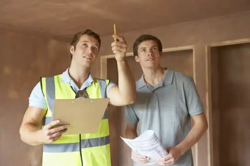 Mann med takstutdanning ser på bygningskonstruksjon med huseier og peker